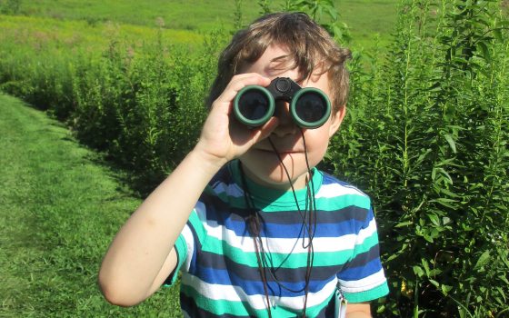 Boy in the Meadow Garden with binoculars on his eyes facing the camera 