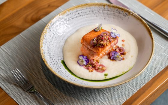 Closeup of place setting with bowl of cooked fish embellished with flowers.