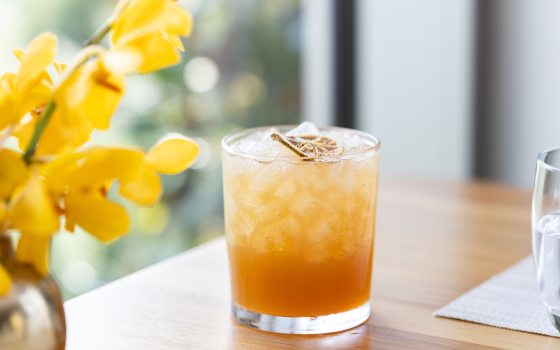 A autumn inspired cocktail in a highball glass, on a light wood table. 