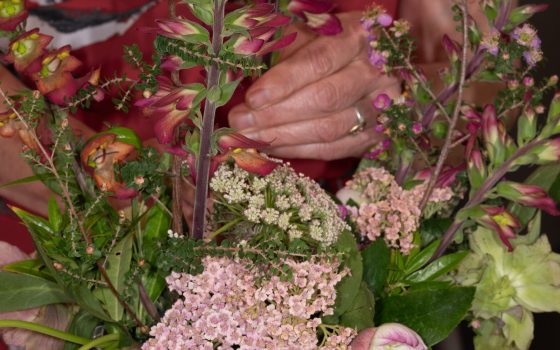 An upclose image of a person's hand arranging stems in a floral arrangement.