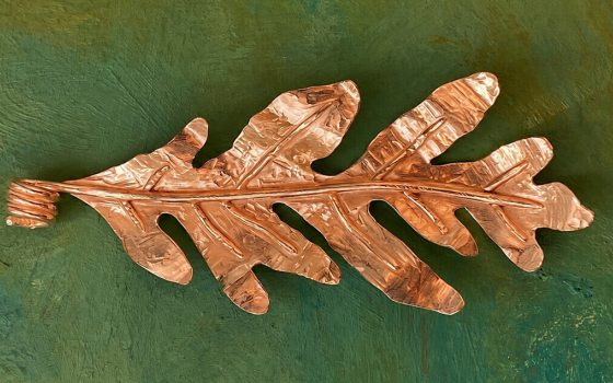 One leaf made out of copper on a green background