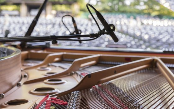 Closeup of a piano opened to show strings, with empty outdoor audience seats in the background.