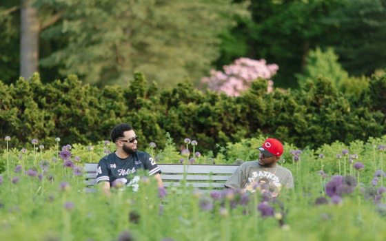 Two people sitting on a wooden bench, talking, at a garden.