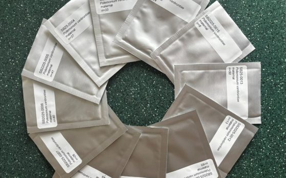 Twelve silver foil seed packets labeled with botanical names arranged in a complete circle on a dark green countertop.