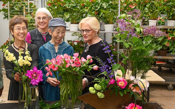 Four floral designers smile broadly at the floral creations in front of them.