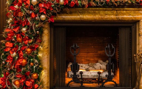 fireplace hearth with a large cascading wreath filled with ornaments, bows, and fabrics  