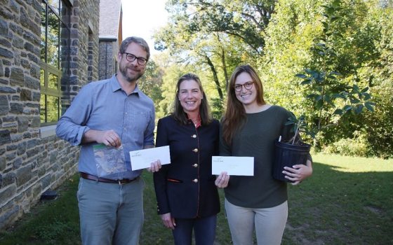 three standing and smiling for the camera while holding up seeds and plants