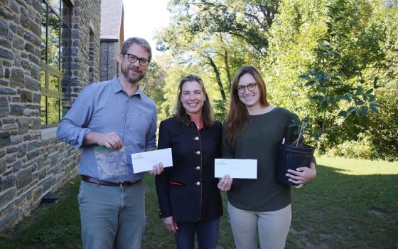 three standing and smiling for the camera while holding up seeds and plants 