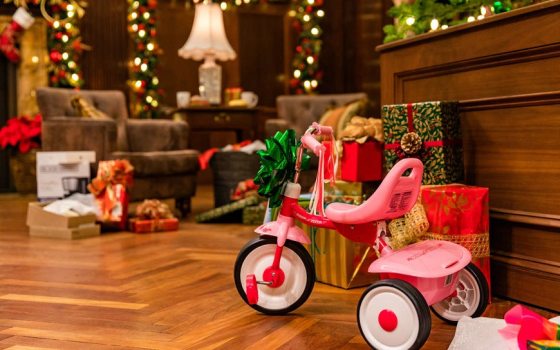 a pink tricycle with a green bowl on it and wrapped presents in the background 