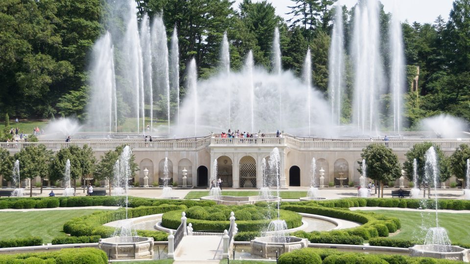 A large display of fountains shoots skyward above a stone facade, with green gardens and smaller fountains in the foreground.