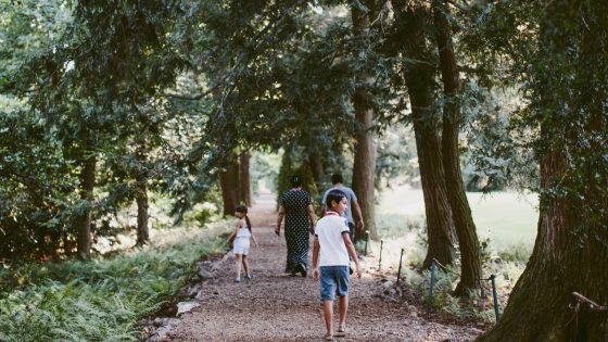 An adult and two children run along a wood chip path lines by large trees
