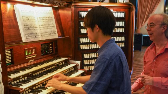 an instructor stands next to a student at the organ console