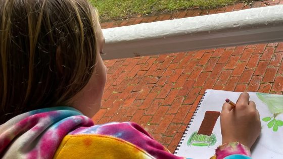 a person in a colorful tie-dye hoodie draws with a pencil in a spiral sketchbook