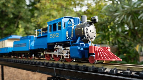 a blue engine—with the number 592, red wheels, and a red cowcatcher—pulls a miniature train along an elevated outdoor track