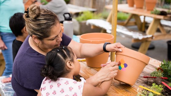 an adult and child paint a multi-colored flower on a large clay pot