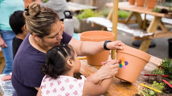 an adult and child paint a multi-colored flower on a large clay pot