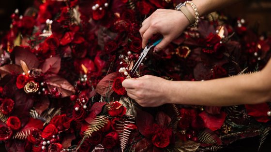 a person with pliers near a floral bouquet of red and gold flowers and leaves