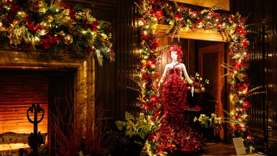 a mannequin in a dress made of red floral material placed in an alcove with christmas garland around it