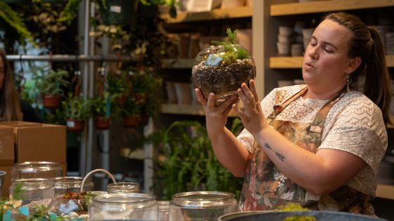 a person surrounded by plant containers holding a terrarium in their hands