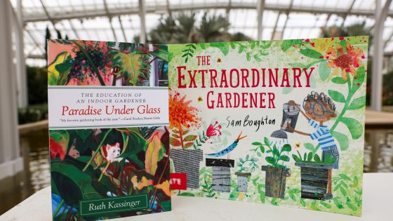 Two colorful books—entitled "Paradise Under Glass" and "The Extraordinary Gardener"—stand on a stone wall with a glimpse of tropical plants in the background, all beneath a glass ceiling.