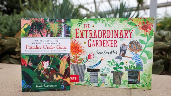 Two colorful books—entitled "Paradise Under Glass" and "The Extraordinary Gardener"—stand on a stone wall with a glimpse of tropical plants in the background, all beneath a glass ceiling.