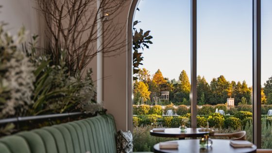 The interior of a restaurant featuring a sage green couch and tall arched ceilings. 