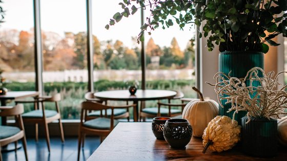 A counter decorated with candles, gourds, and a large teal vase of greenery gives way to tables in front of arched windows overlooking a fountain garden.