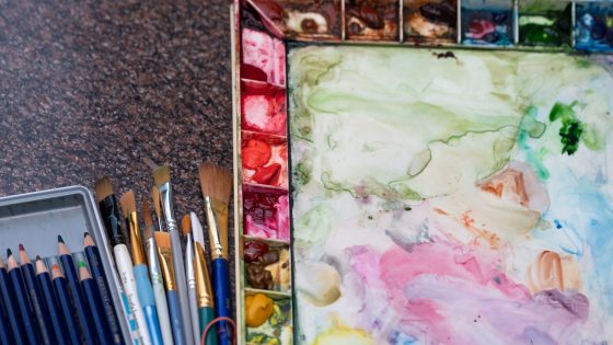 A watercolor and paint palette next to paint brushes.