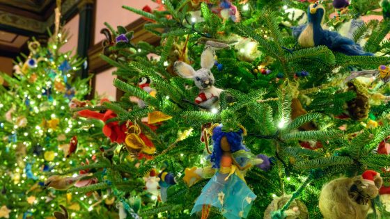A vertical shot of a heavily decorated Christmas tree. The ornaments are unique, including a central needle-felted white rabbit with a red scarf, a figure with a blue fabric skirt, a felted blue bird, and various other whimsical animal ornaments.