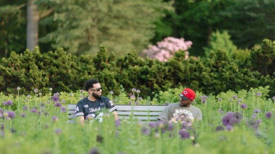 Two people sitting on a wooden bench, talking, at a garden.