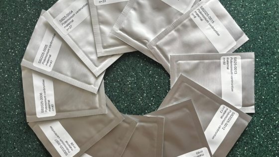 Twelve silver foil seed packets labeled with botanical names arranged in a complete circle on a dark green countertop.