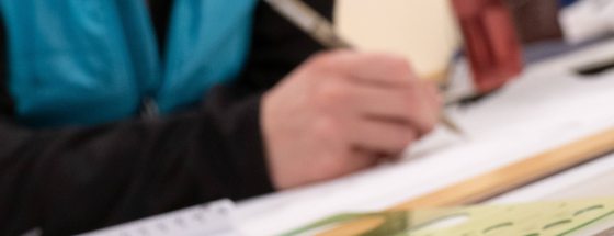 closeup of hand sketching on an inclined surface with drafting tools nearby