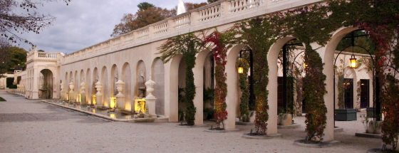 long view of stone archways; covered by vines in the forefront and backed by fountains as the view recedes