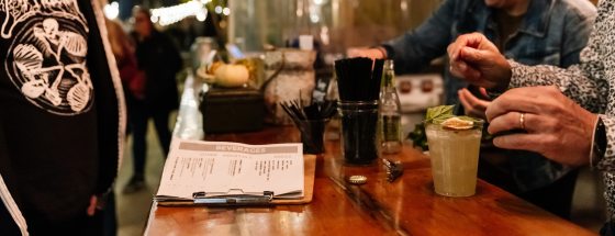 a bartender serves botanically-inspired cocktails to two people at an outdoor bar