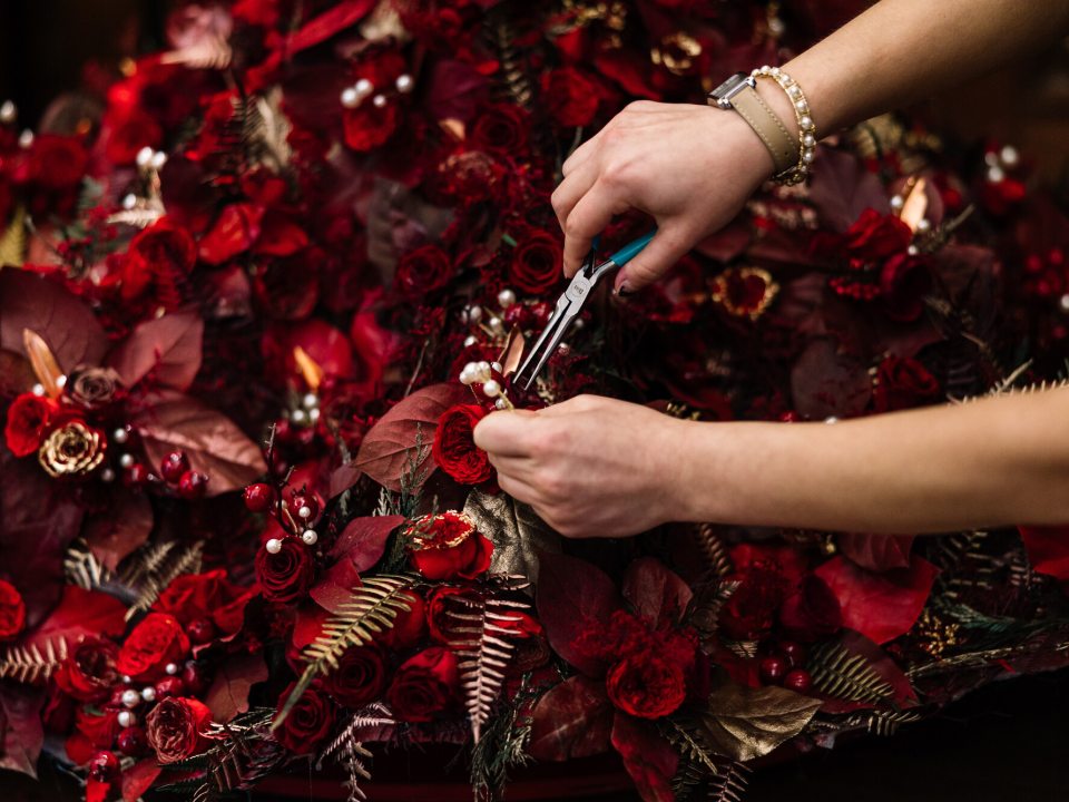 a person with pliers near a floral bouquet of red and gold flowers and leaves