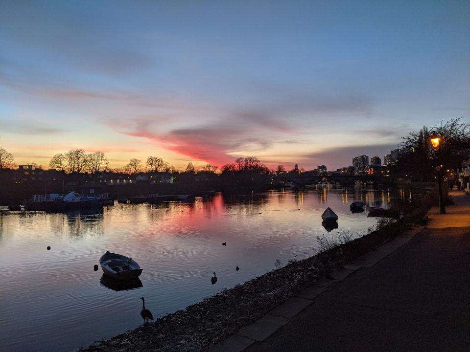 A sunset image over a river with small boats and geese wading.