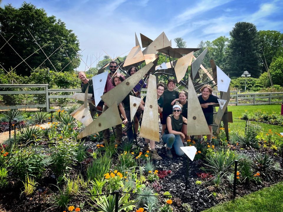 A group of people standing inside an outdoor geometric sculpture in a garden bed.