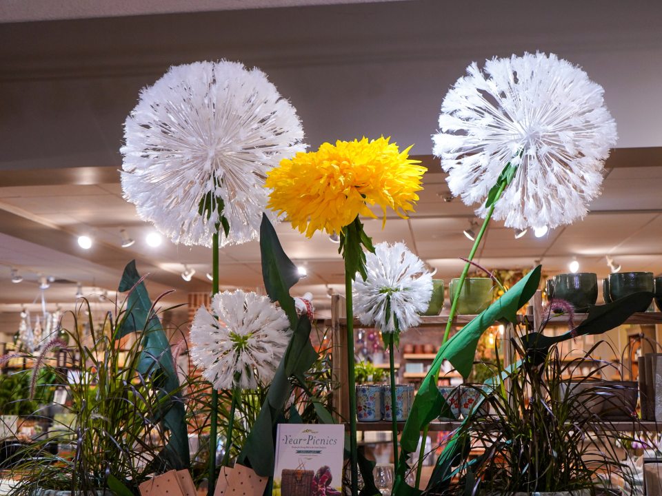 Large handmade paper flowers in yellow and white hanging in a gift shop.