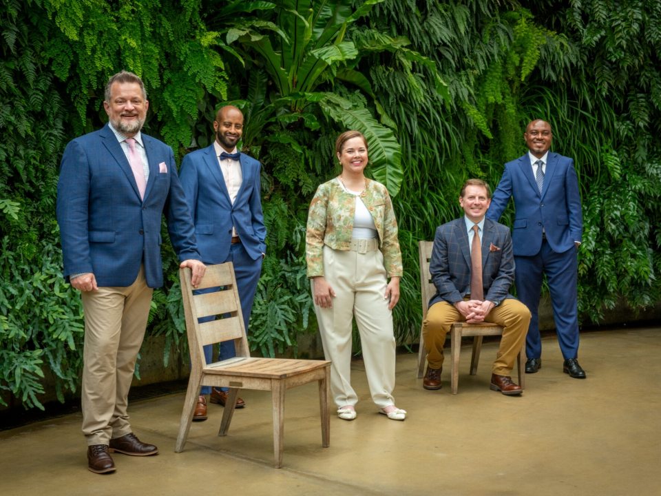 A group of five people posed in front of a green wall smiling at the camera.