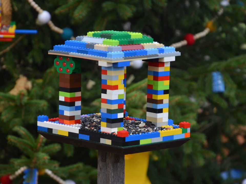 A birdhouse made from lego blocks hanging on an outdoor evergreen tree.