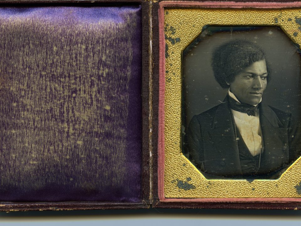 An old frame containing a black and white image of a person in a tuxedo, surrounded by a gold inset on the frame.