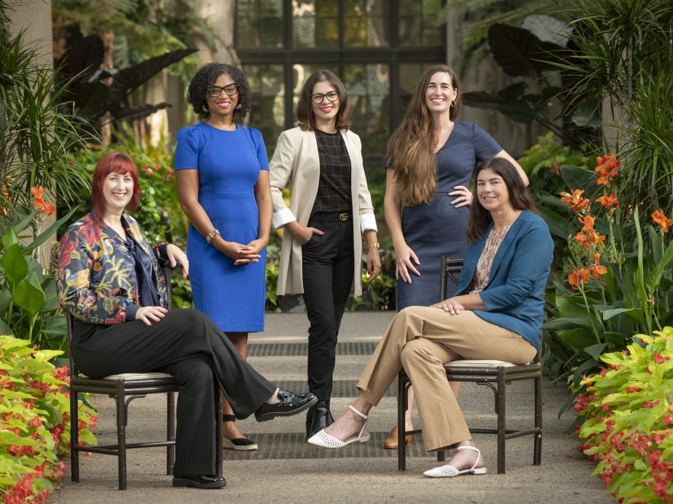 A group of 5 people, some sitting, some standing, in a garden setting.