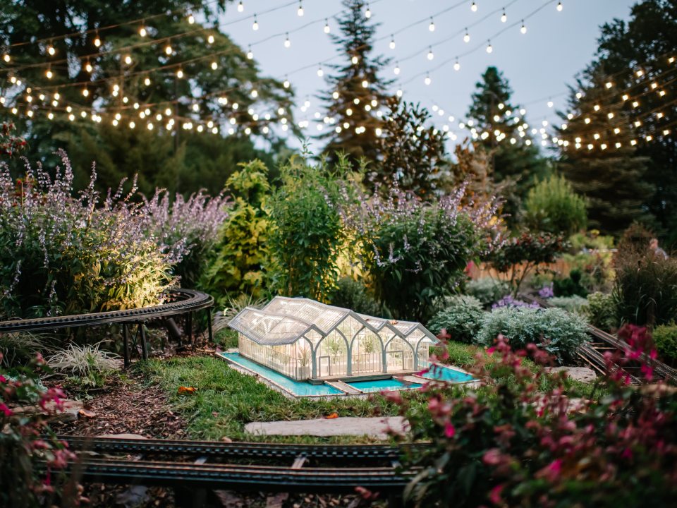 A model of a glass conservatory sitting in an outdoor model train display.