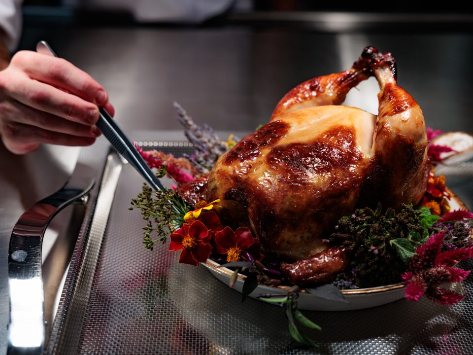 A person plating a whole roasted chicken on top of a bed of flowers. 
