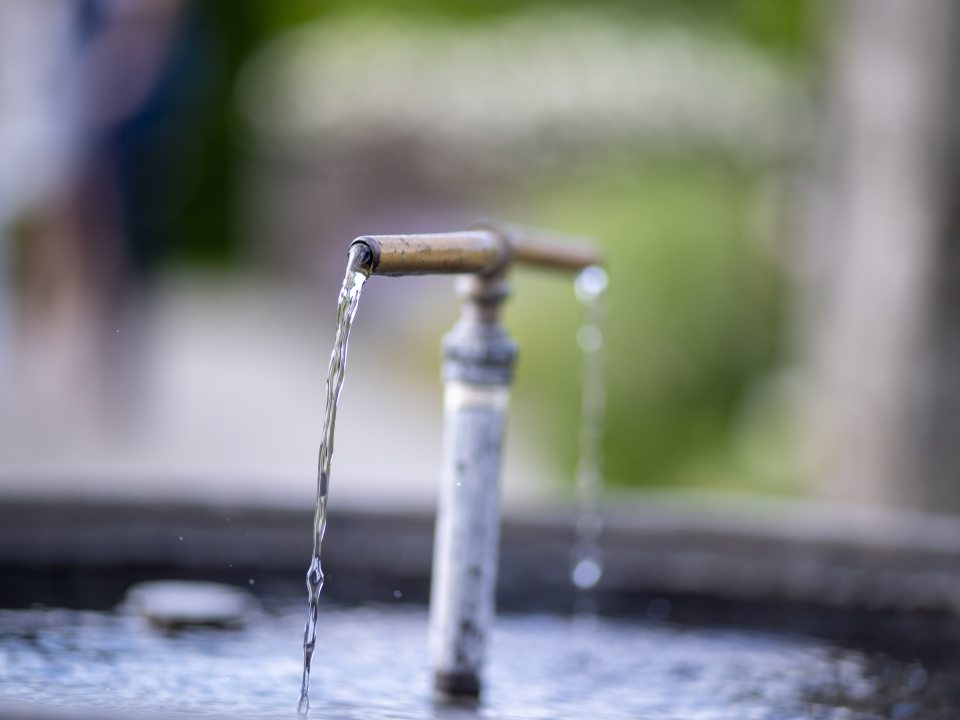 A t-shaped water fountain, with water coming our of both ends of the "t" into a pot. 