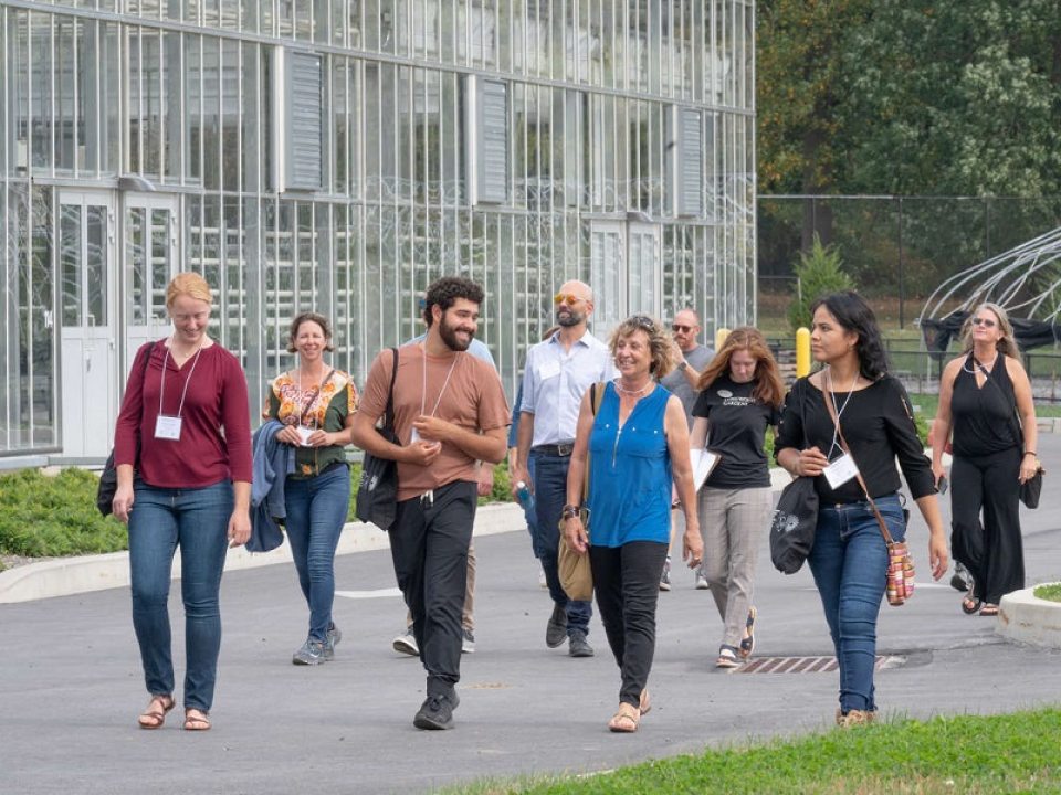 a group of people smiling and walking next to a glass greenhouse 