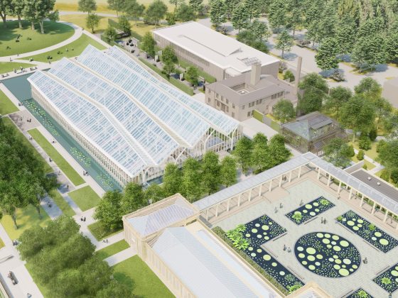 Overhead view of large glass house with 3-peaked roof, oval and rectangular pools dotted with plants, amid lush green lawns and trees