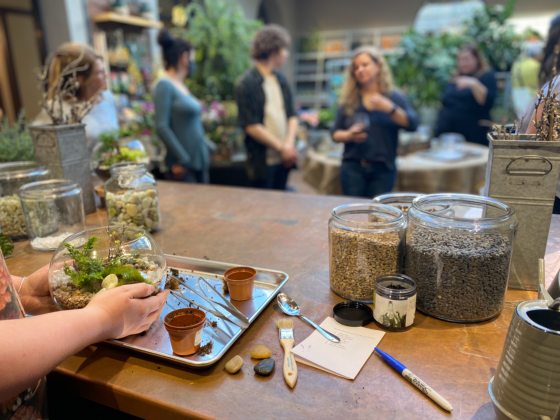a set of hands holding a terrarium with a group of people talking in the background 