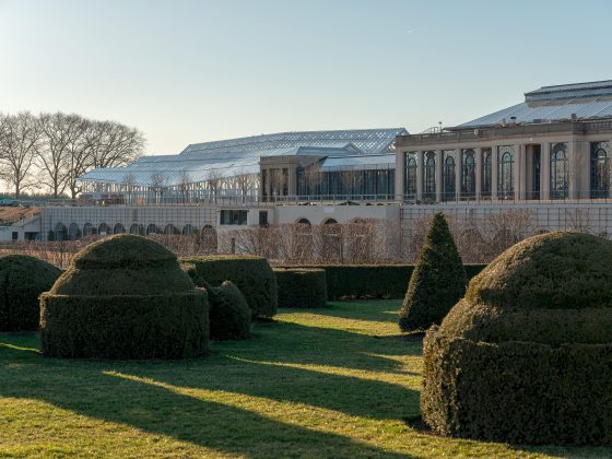 a sprawling glasshouse sits on a ridge above pruned topairies