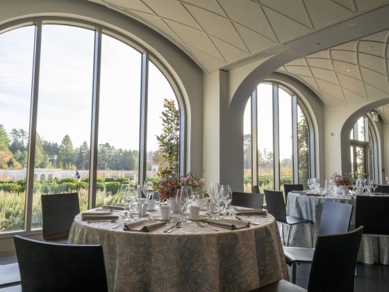Tables set for fine dining look out through arched windows to a view of the gardens beyond.